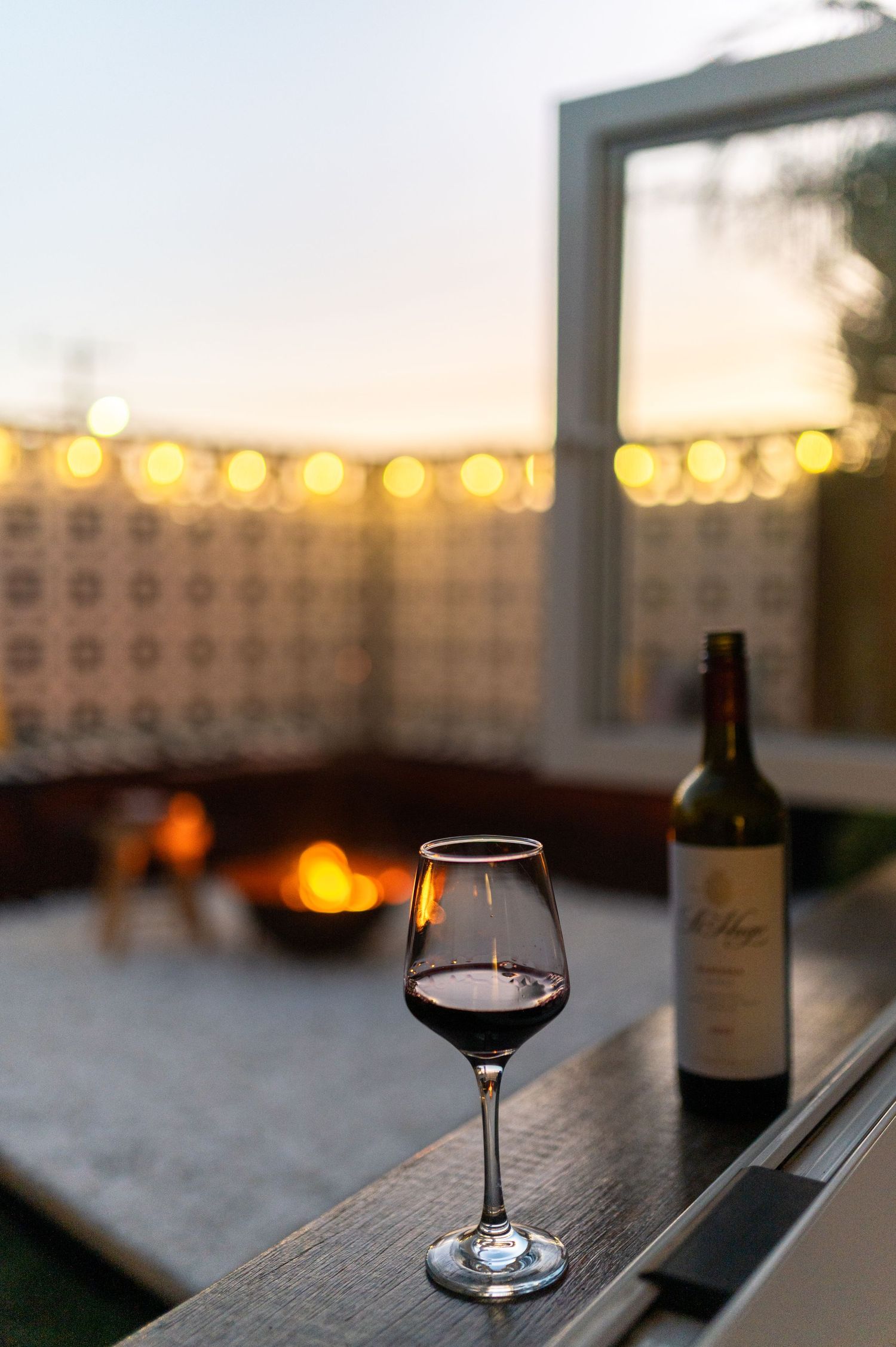 A gift box tied with a white ribbon sits beside two glasses of red wine on a wooden table near a yellow door.