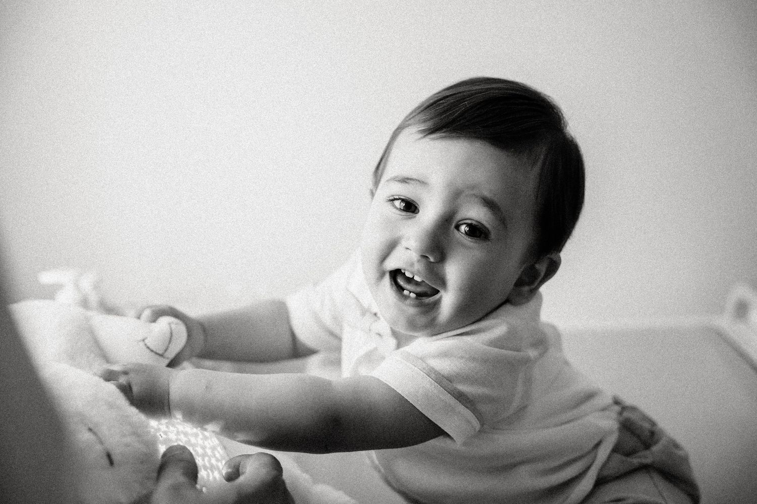 Happy baby smiling and playing, black and white portrait photo of joyful infant in white outfit.