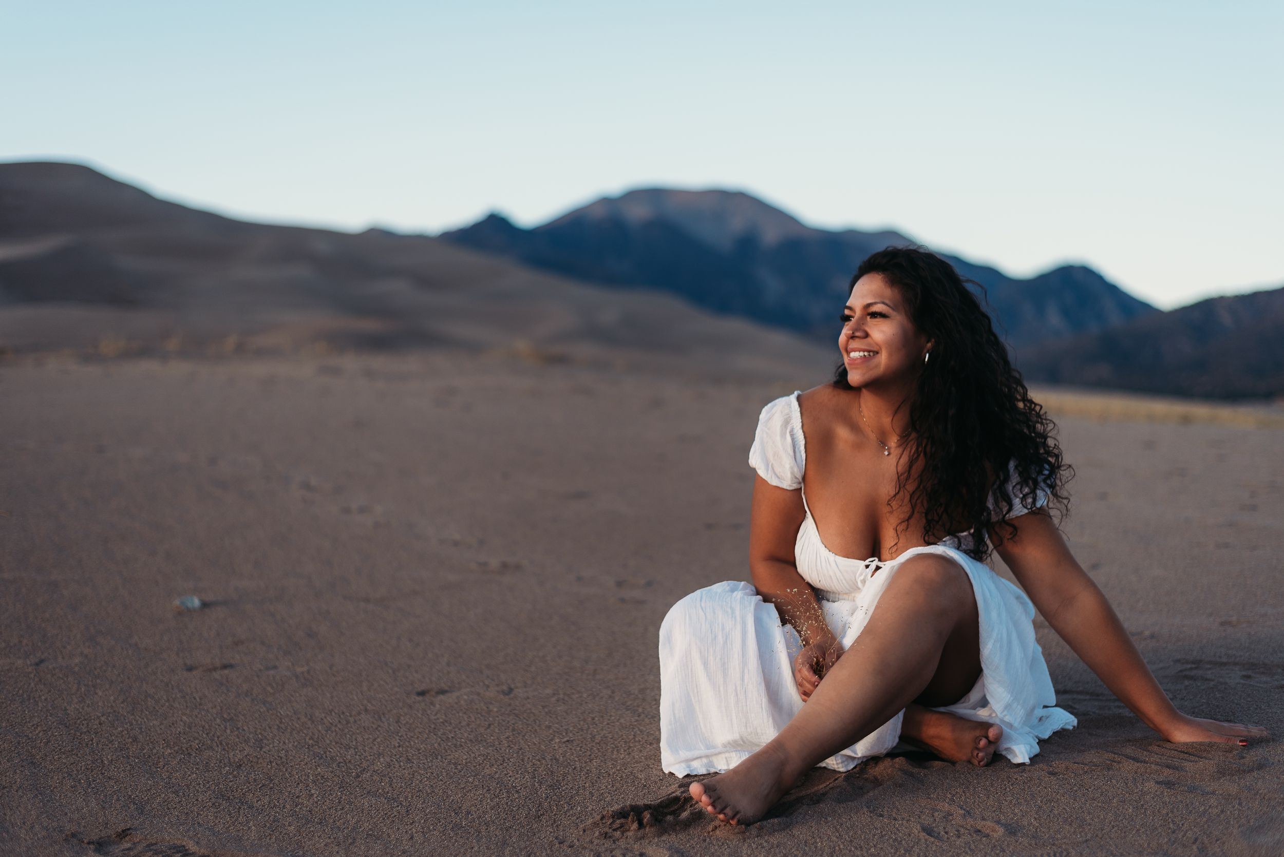 woman sitting cross legged on sand with Colorado mountains in the background.