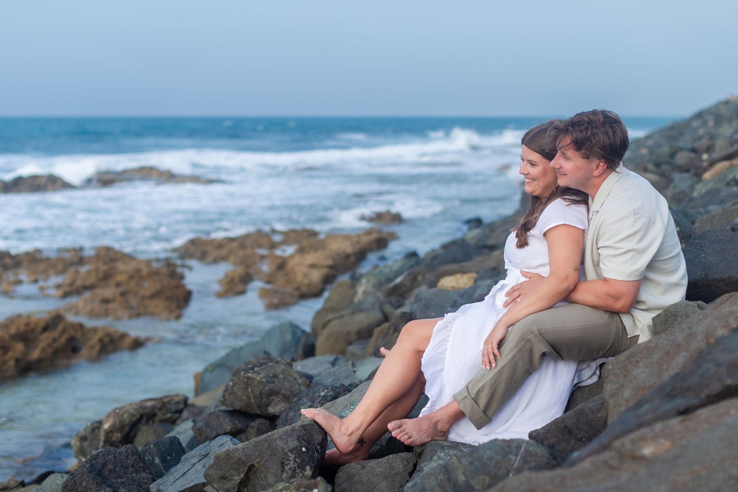 Couples portrait seated on the rocks at Balneario del Escambrón in Old San Juan, Puerto Rico.