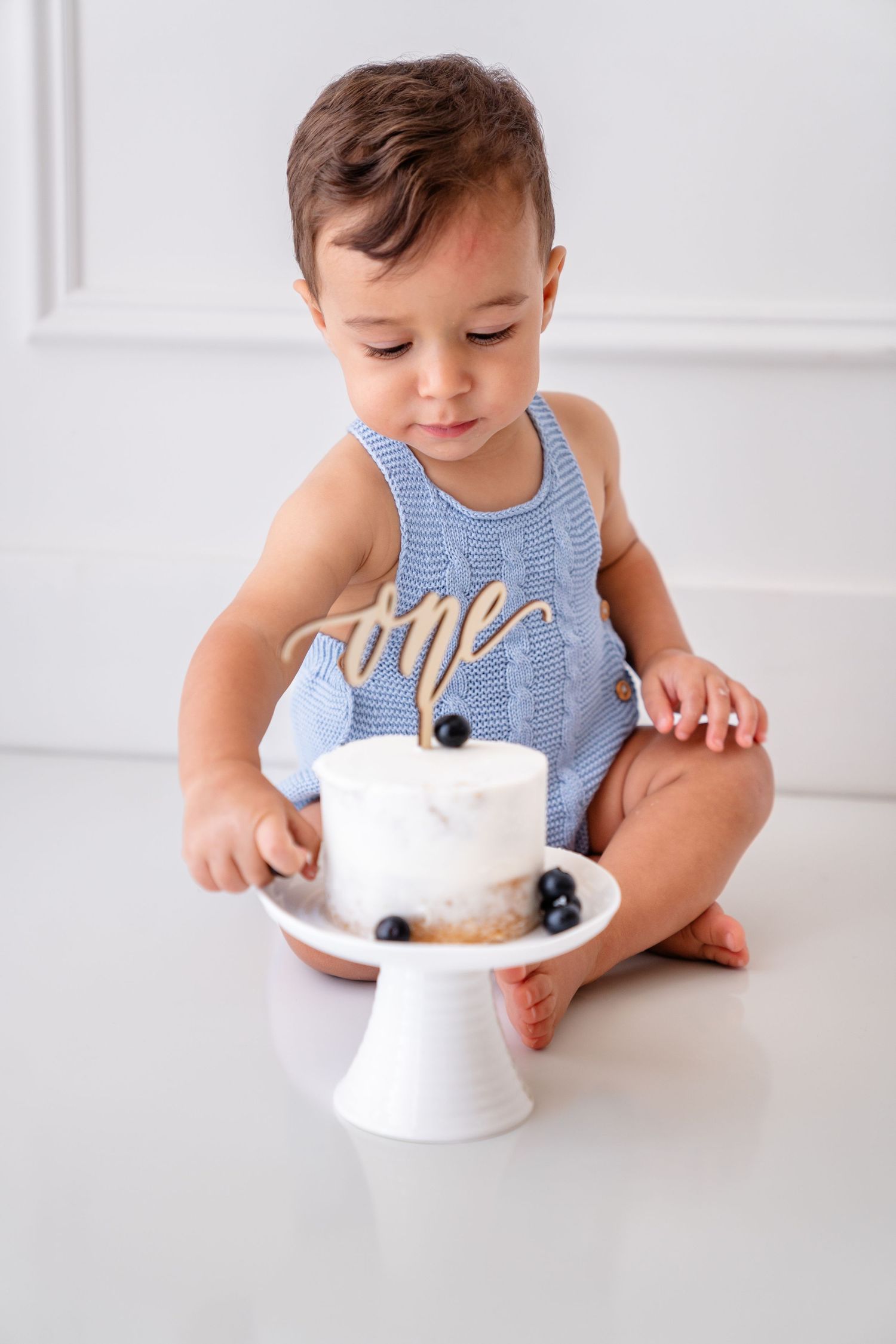 Adorable baby girl in lace dress eating smash cake with colorful sprinkles during first birthday photo session.