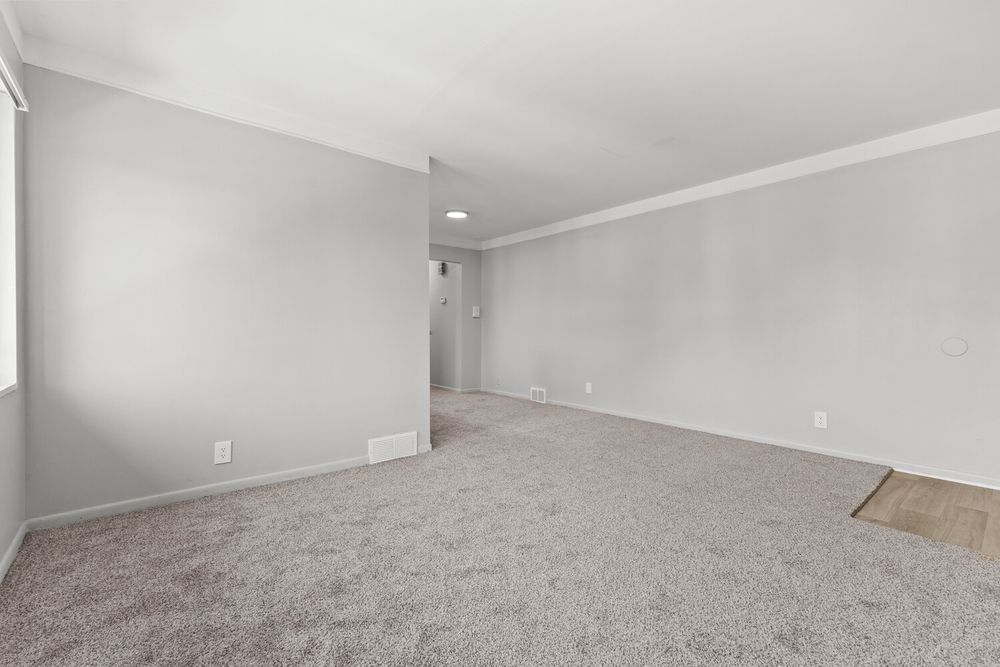 Empty carpeted room with gray walls, crown molding, and neutral tones in a residential space.