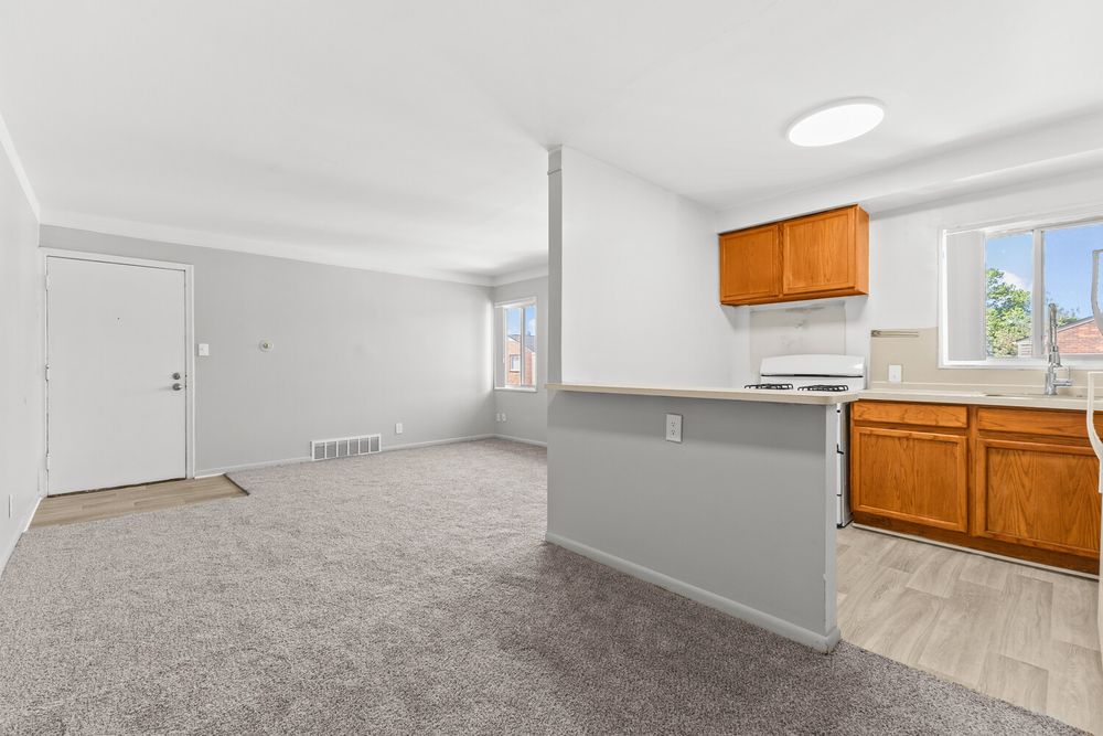 Open kitchen with oak cabinets, white appliances, peninsula counter, and carpeted living area beyond.