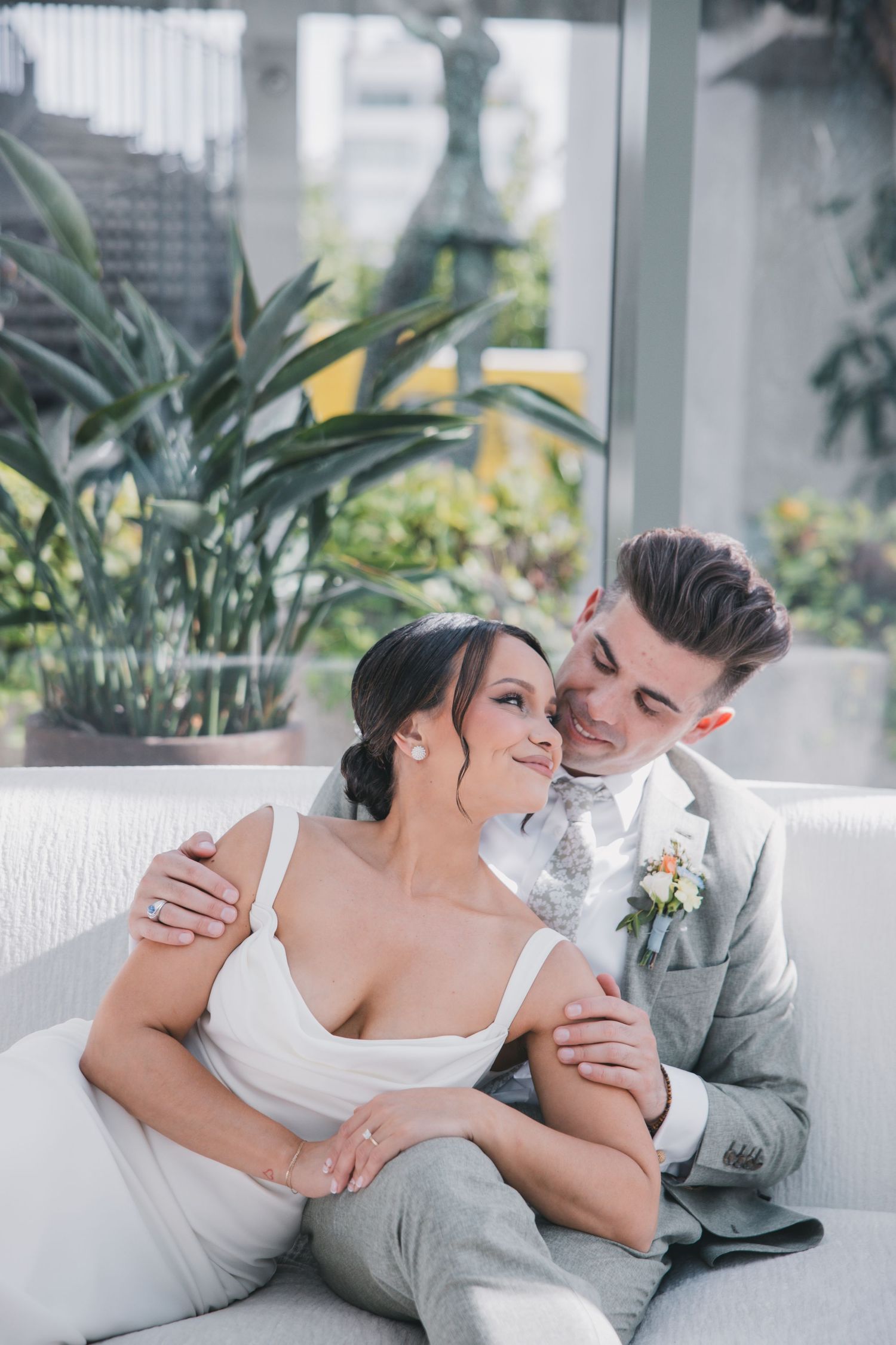 Bride in white gown holding colorful bouquet stands with groom in sage suit against cloudy sky.