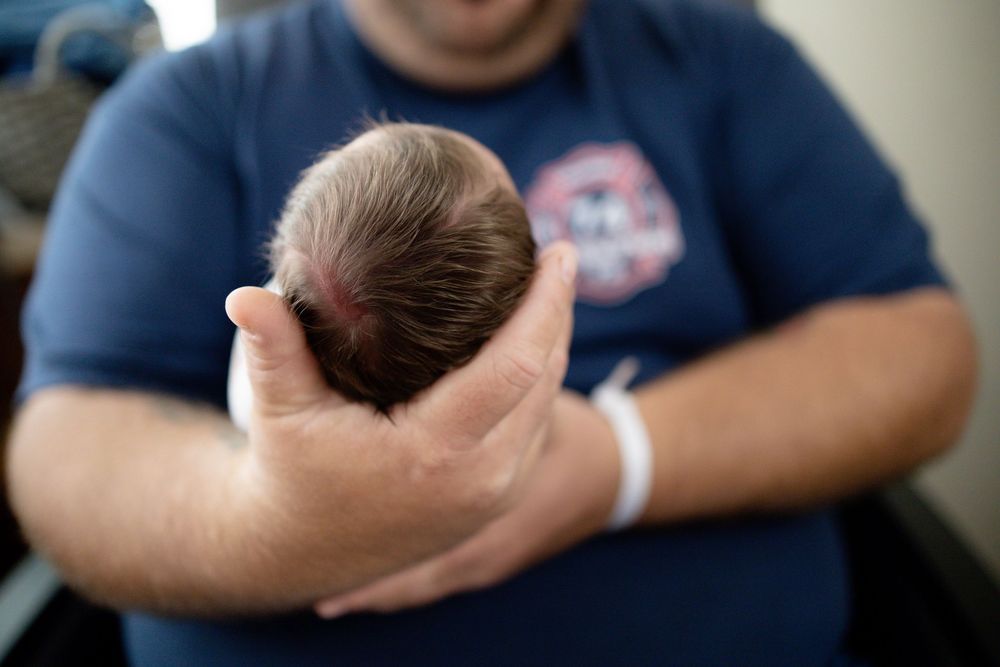 Man in blue shirt gently cradling a newborn baby's head in his hand.