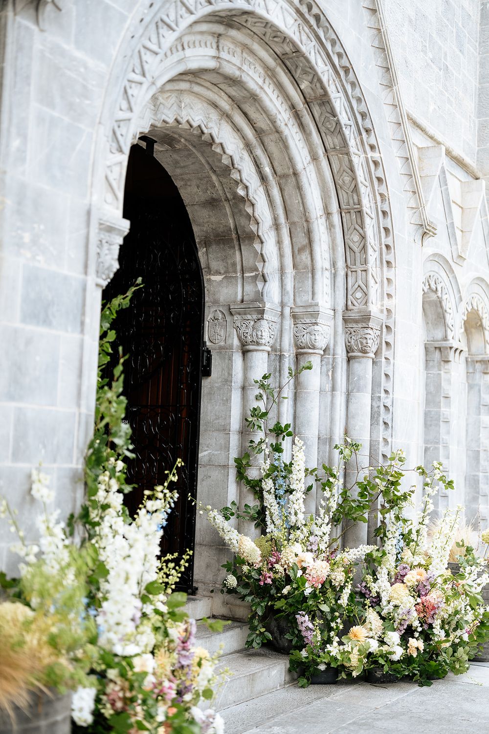 White stone archways of Honan Chapel are decorated with elegant floral arrangements featuring pink and white flowers and greenery.