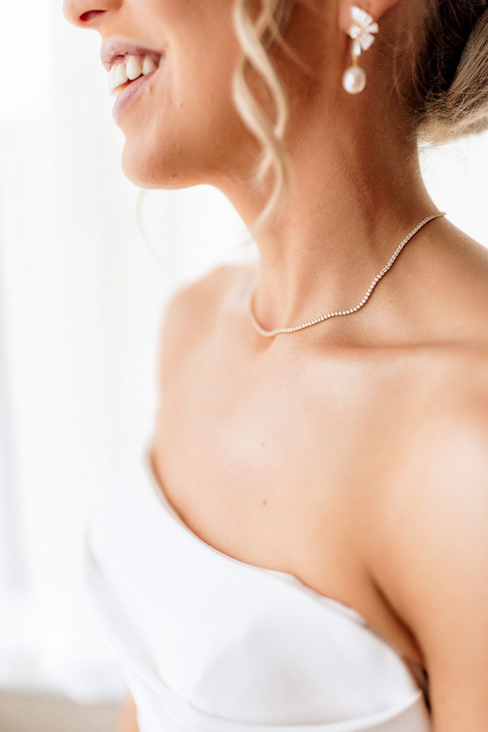 Beautiful bridal details showing delicate jewelry and a stunning white strapless wedding gown against a soft light background.