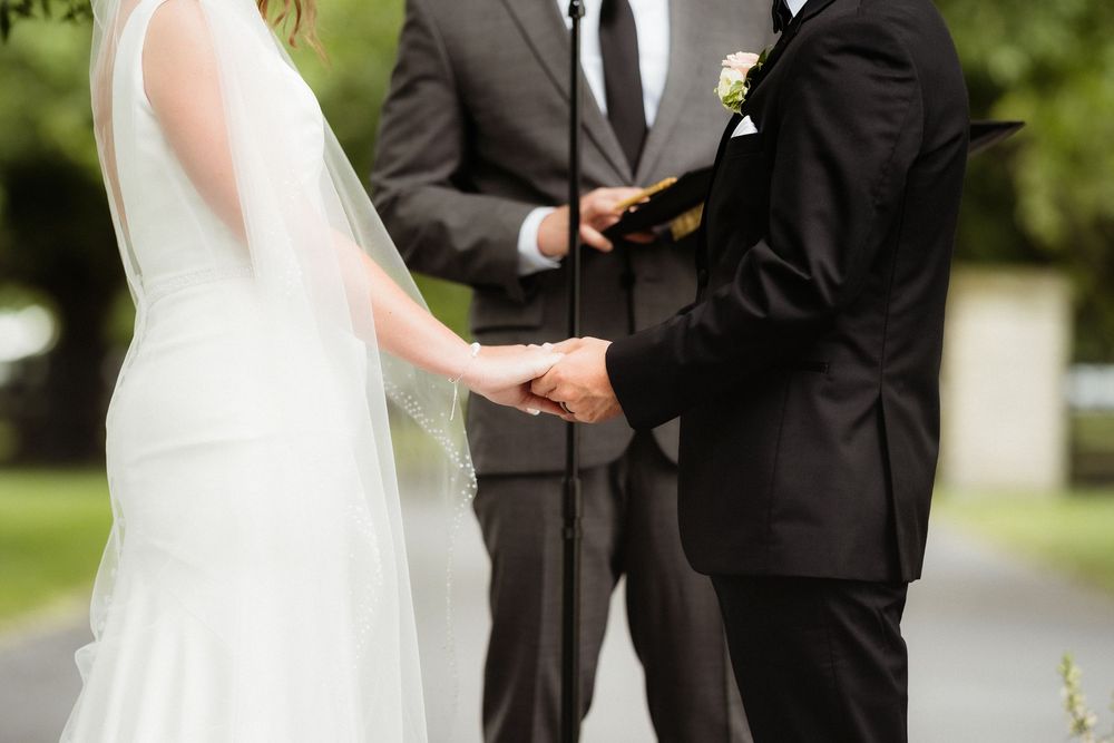 Bride and groom holding hands during outdoor wedding ceremony with officiant reading vows.