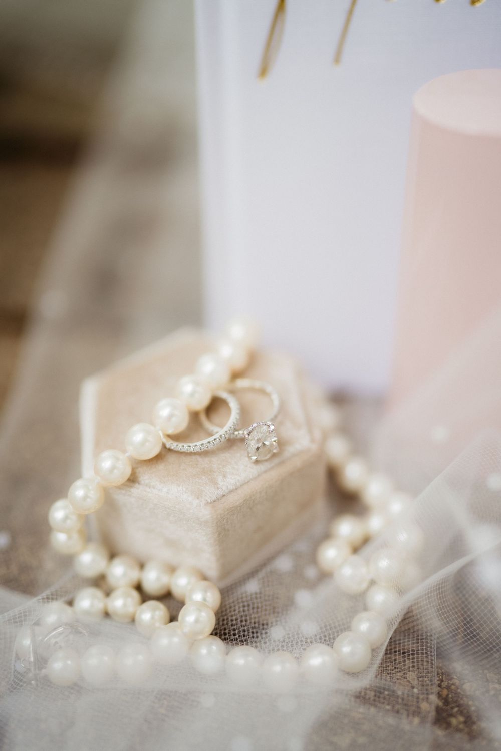 Elegant wedding rings on a velvet box surrounded by a pearl necklace and soft candlelight on a lace veil.
