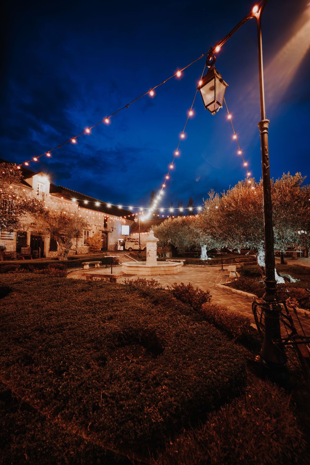 Charming outdoor wedding venue courtyard with string lights and fountain at dusk.
