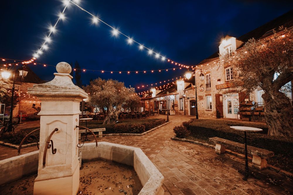 Charming stone courtyard at night illuminated by warm string lights with a decorative fountain centerpiece.