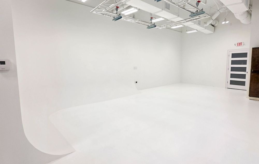 Bright white photography studio with seamless cyclorama wall, professional lighting rigs, and clean open floor space.