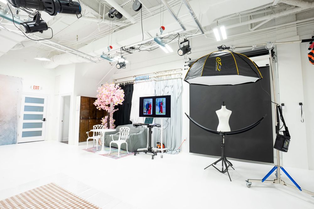 Professional photography studio with white floors, lighting equipment, pink cherry blossom tree, mannequin, and dual monitors on display.
