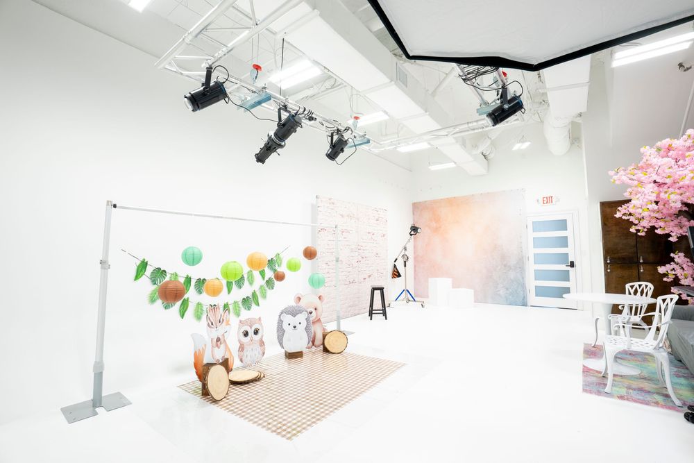 Bright white photography studio with colorful garland, owl props, pastel backdrop, pink cherry blossom tree, and professional lighting.