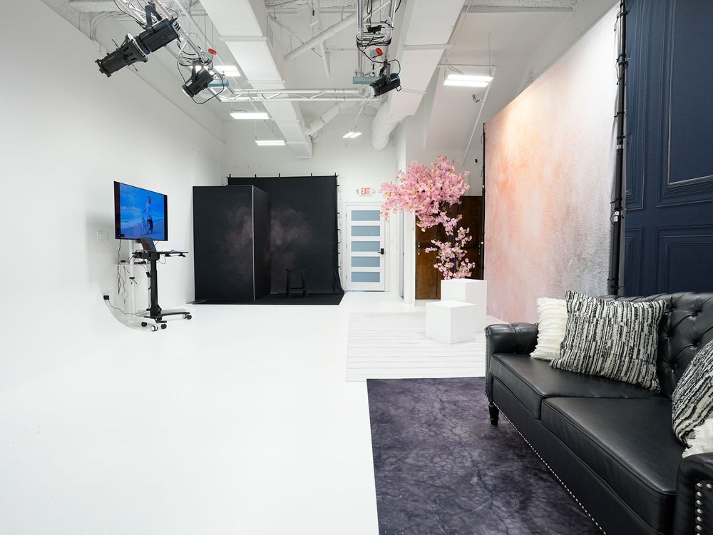Modern photography studio with white cyclorama, black backdrop, LED lighting, leather sofa, and cherry blossom decor.