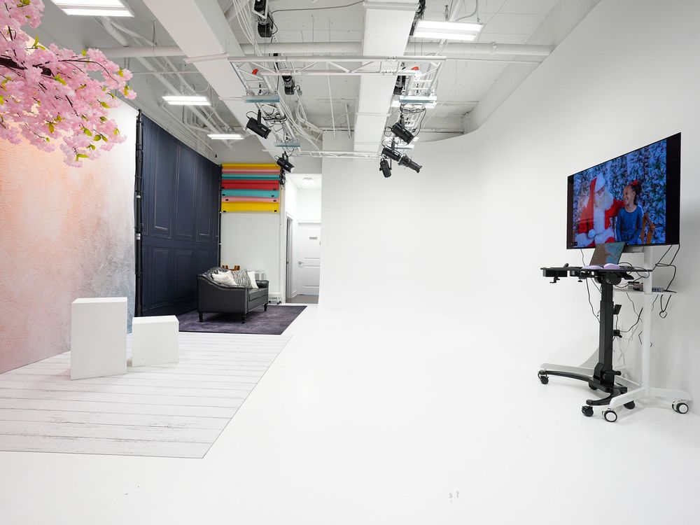 Modern photography studio with white cyclorama wall, studio lights, TV monitor on wheels, and decorative backdrops.