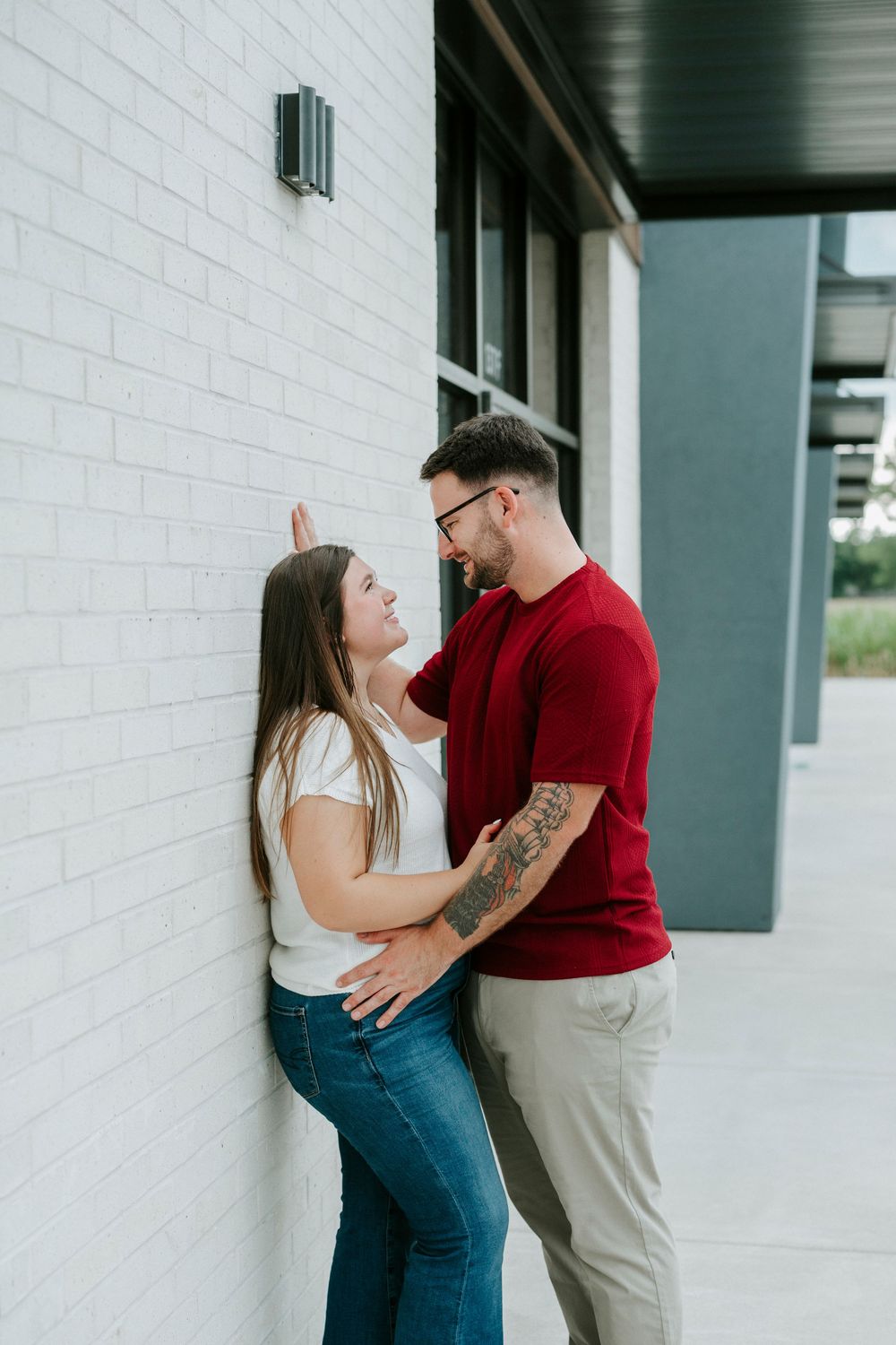 A couple shares a romantic moment against a white brick wall, the man in red shirt gently holding the womans face.