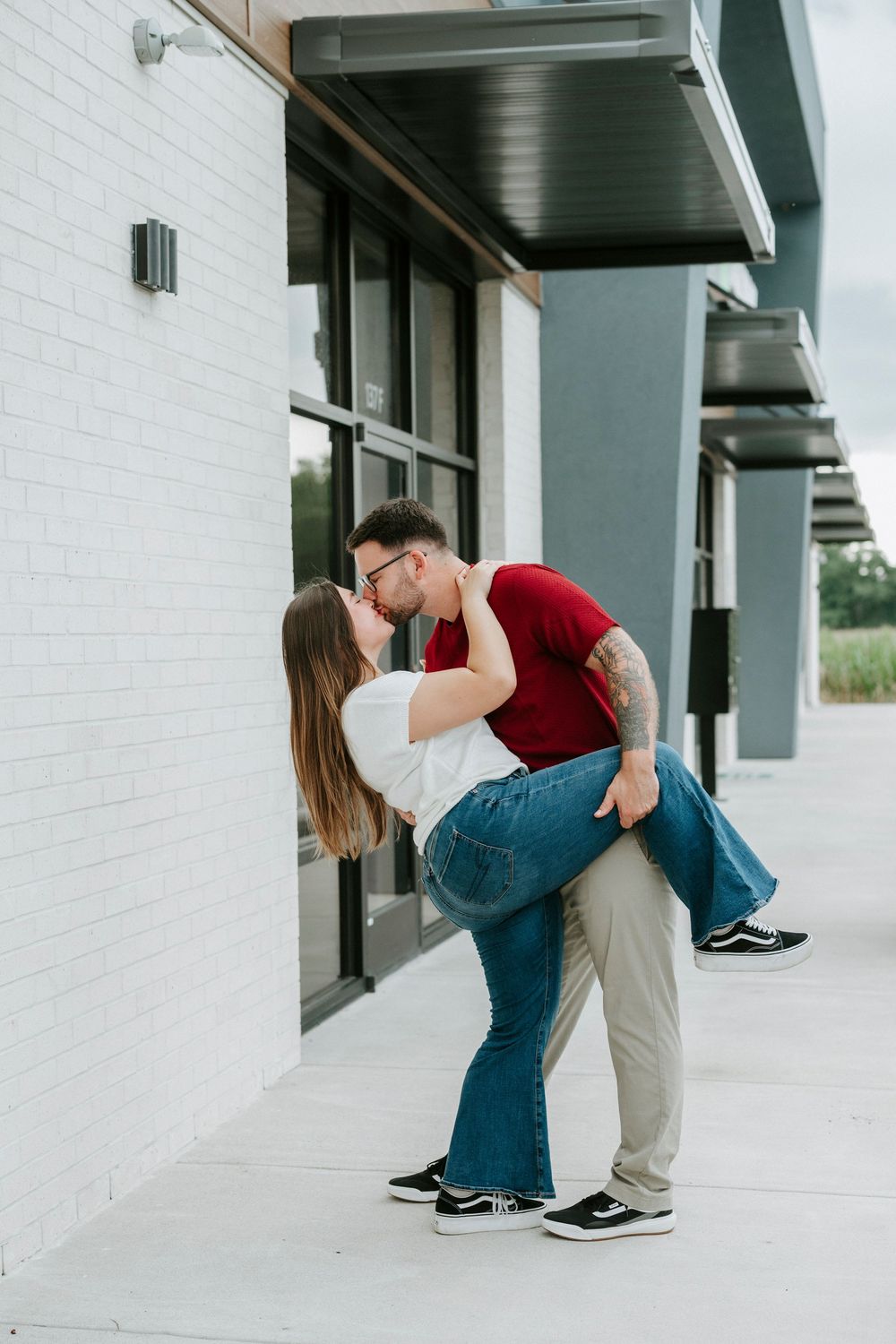 Couple sharing a romantic dip kiss outside a modern building with white brick walls and black windows.