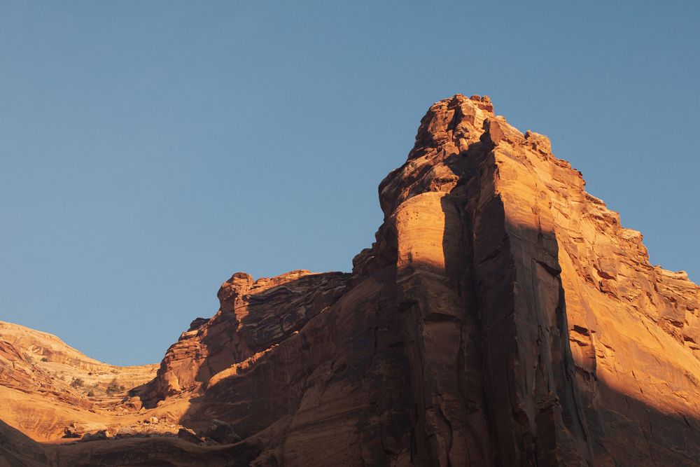 Sunlit red sandstone rock formation against a clear blue sky in a desert canyon landscape.