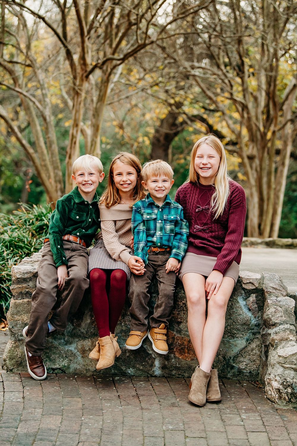 Four siblings sitting on a stone bench in a wooded garden wearing fall coordinated outfits.