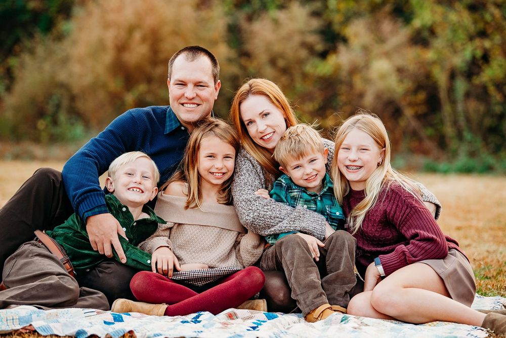Happy family of six smiling together outdoors on a blanket in a fall setting.