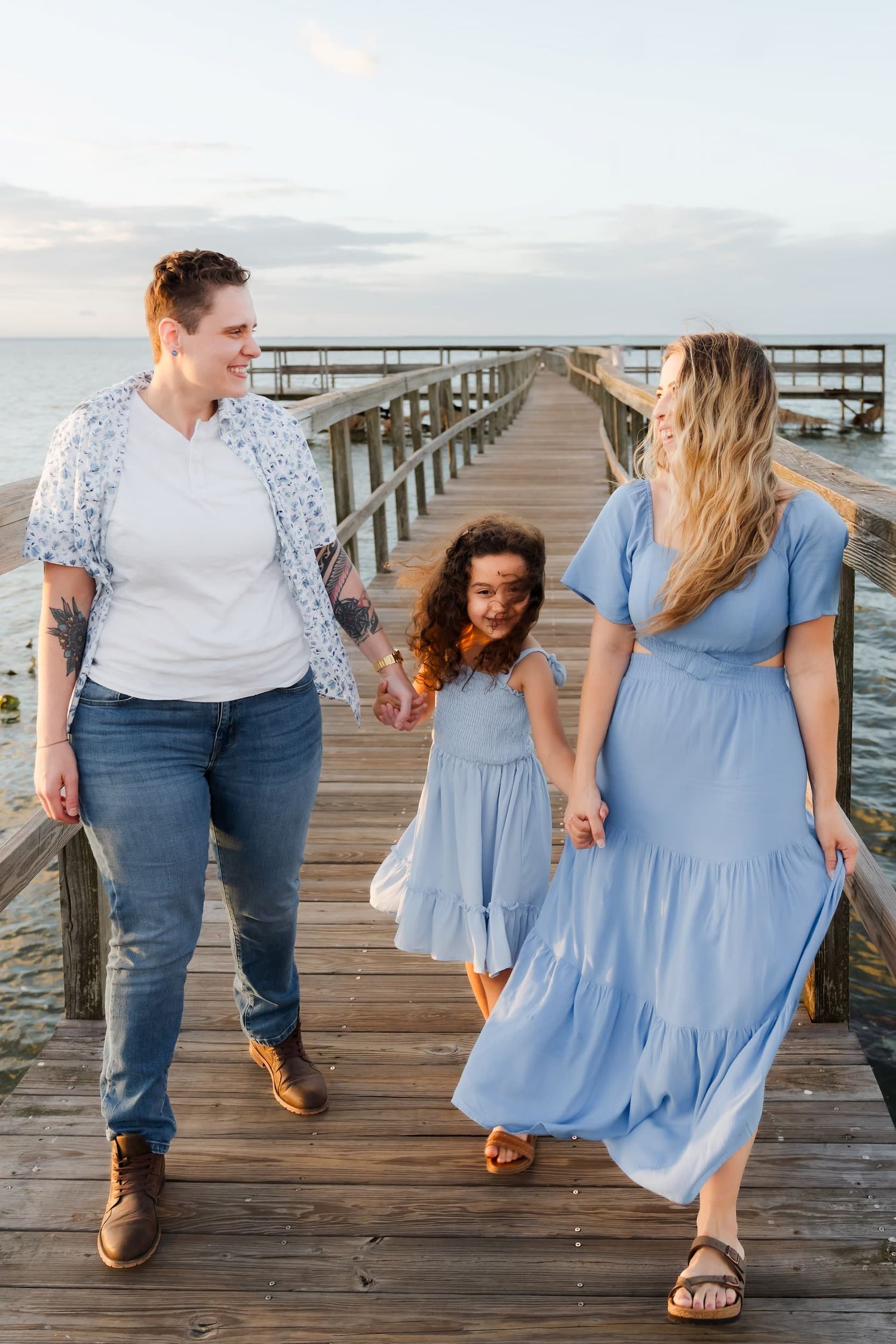 Three people in blue outfits sit together outdoors on a bench during golden hour lighting in a park setting.
