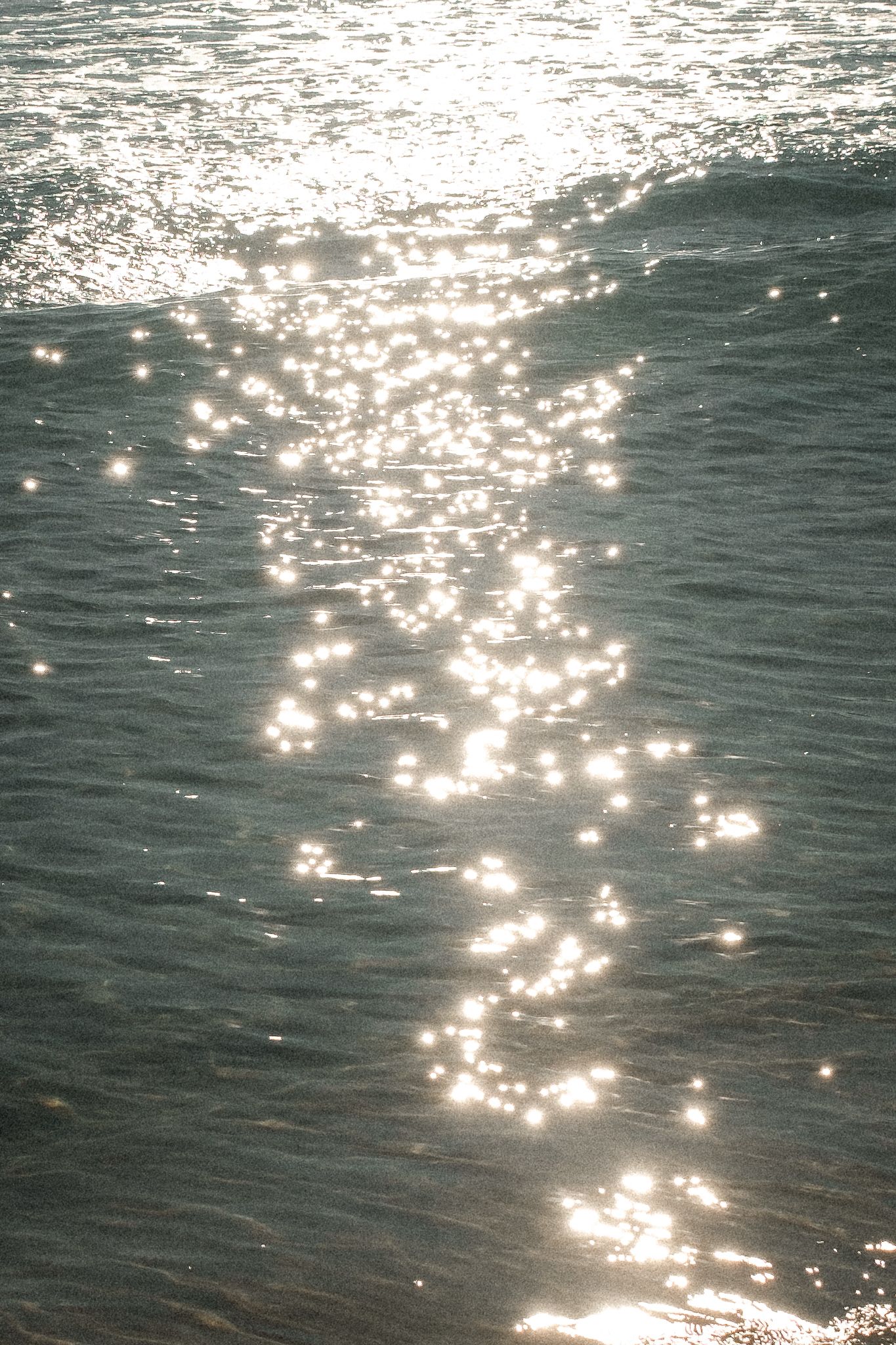 Sunlight sparkles on gently rippling ocean waves, creating a dazzling trail of bright reflections on the water surface.