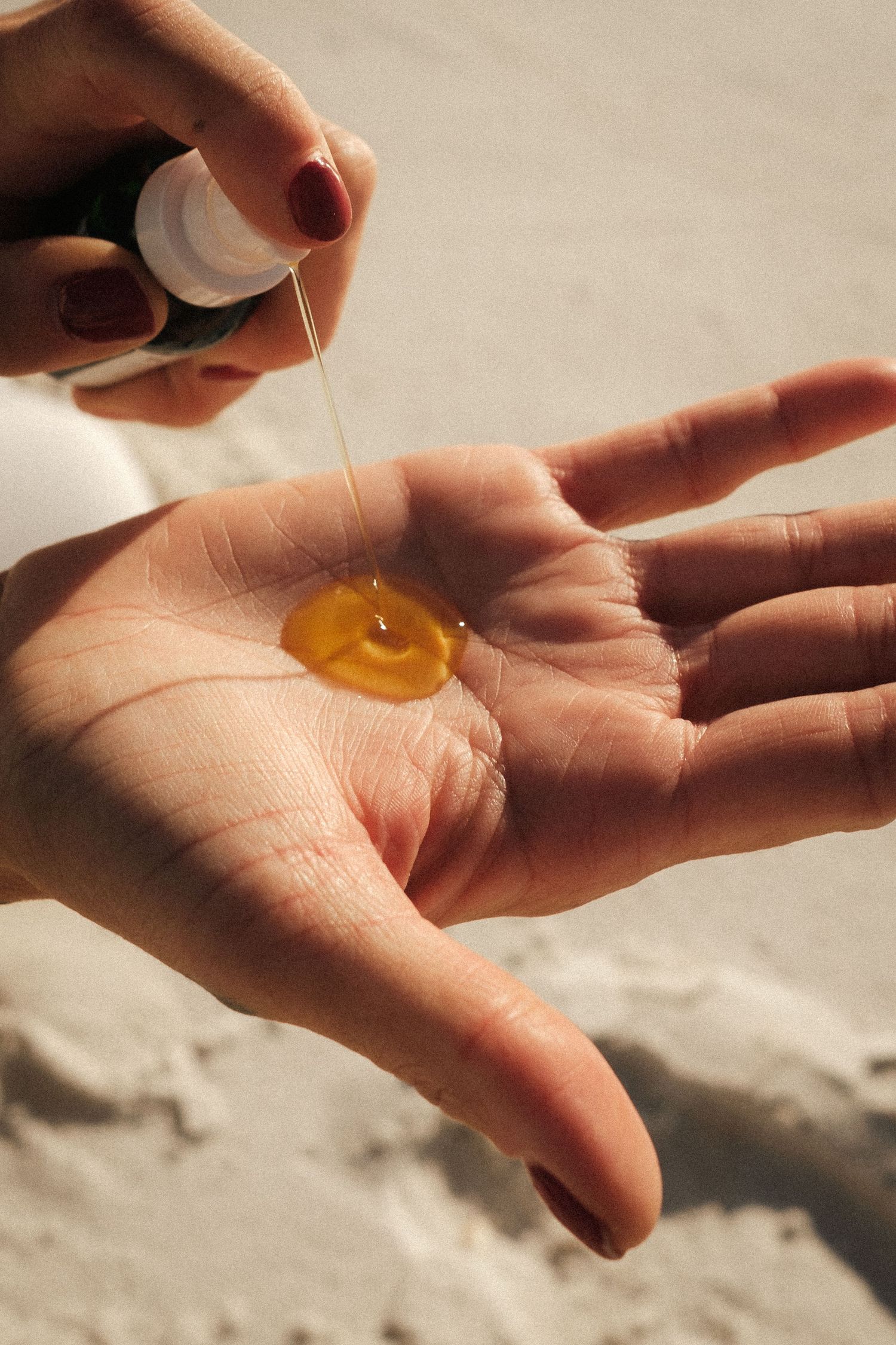 Close-up of golden oil being dropped onto a woman's palm at the beach.