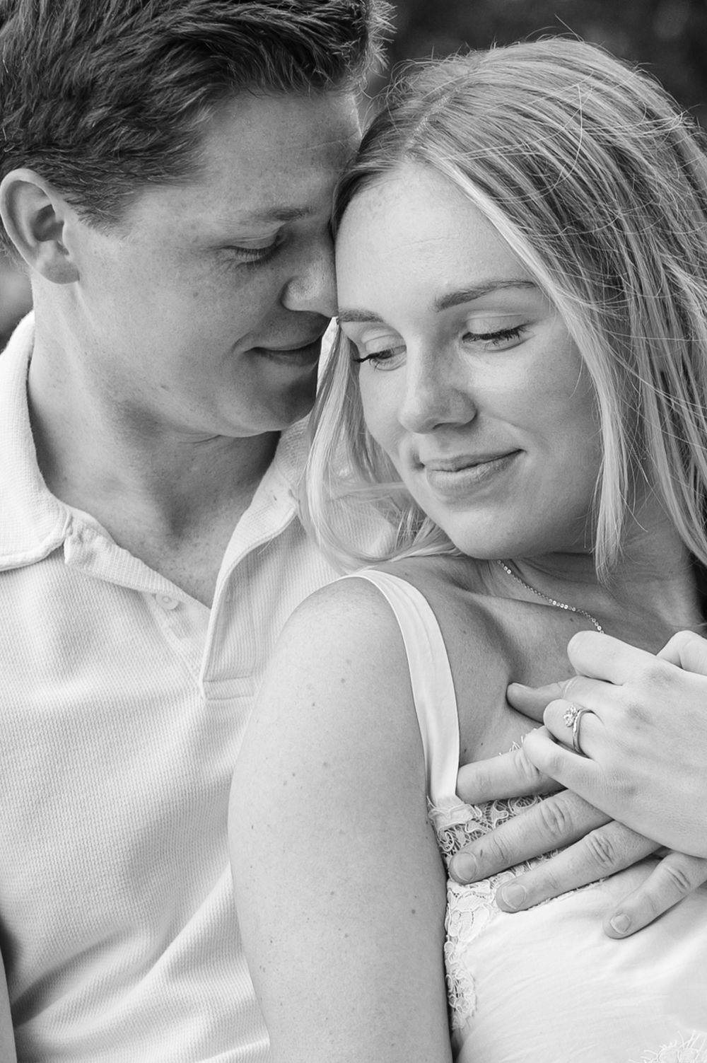 Black and white photo of a couple embracing, woman smiling with engagement ring visible on her hand.