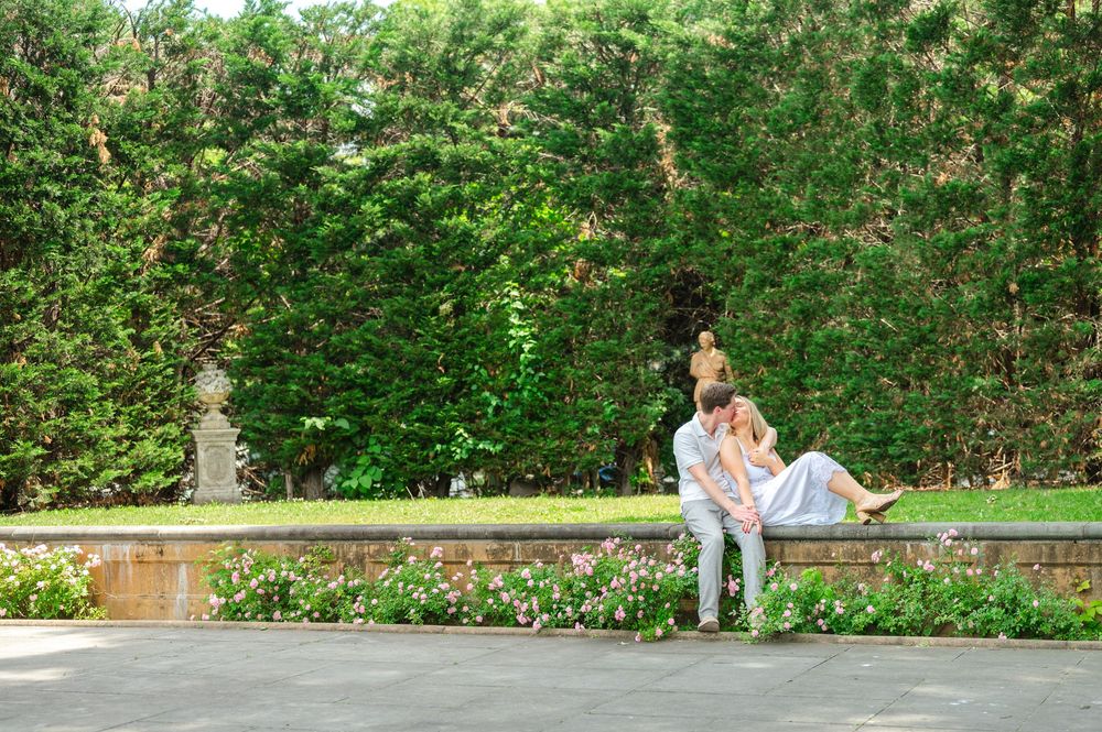 Couple sharing a romantic moment on a garden bench surrounded by lush greenery and blooming flowers.