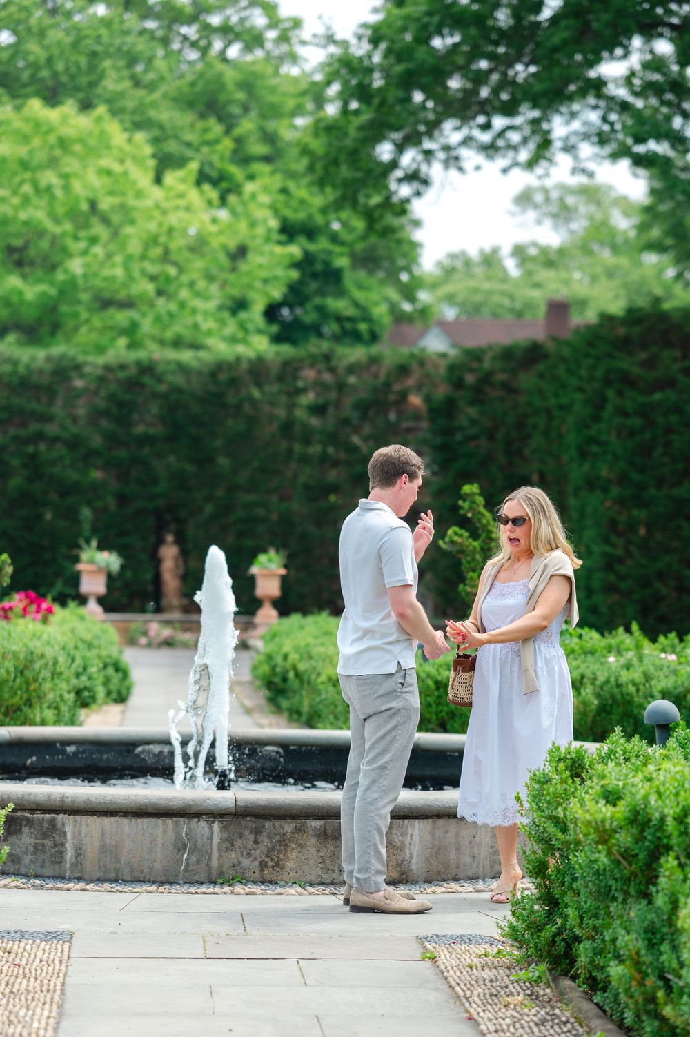 Man showing a ring box to a woman near a garden fountain during a marriage proposal outdoors.