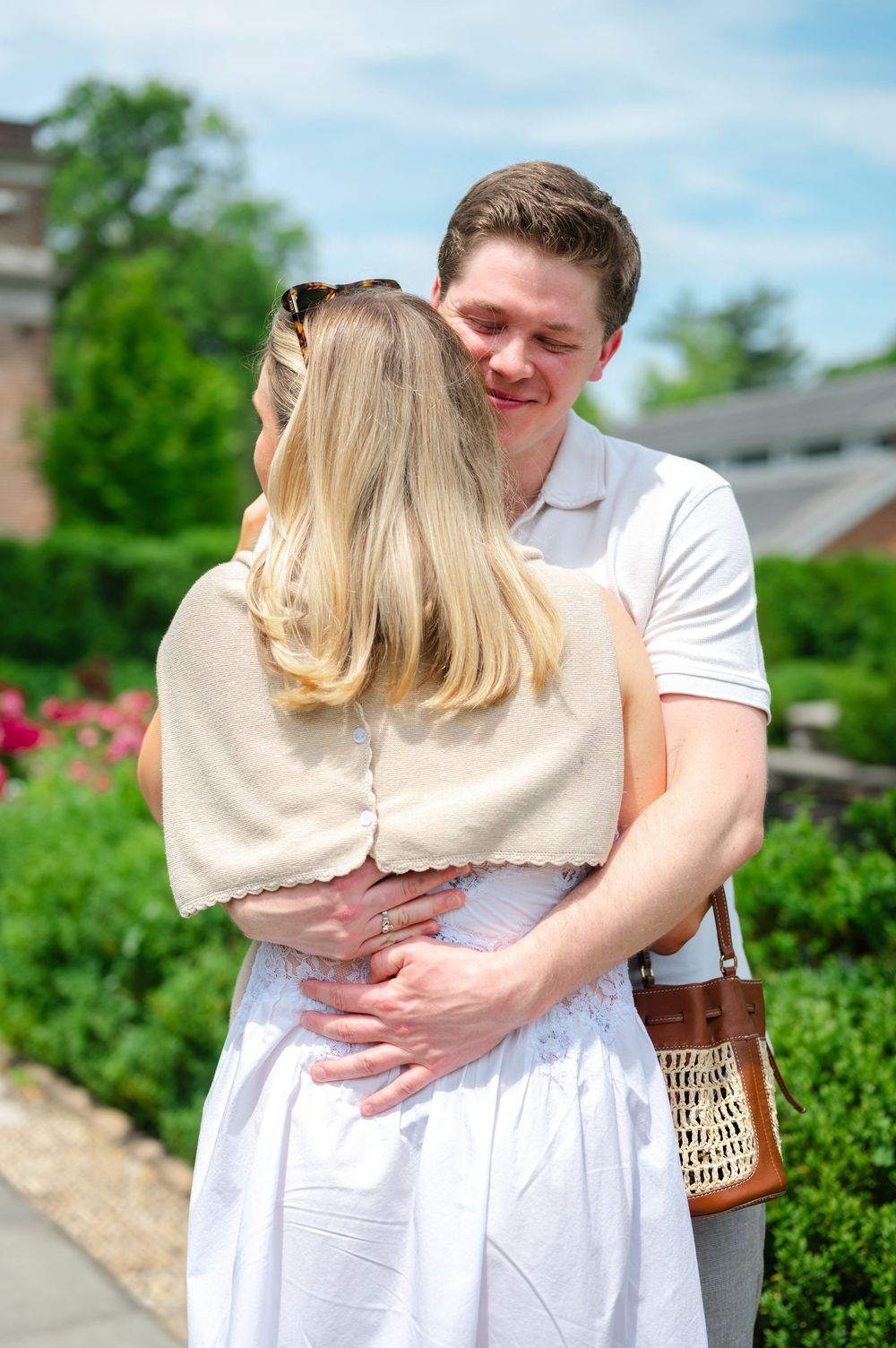 Man embracing a blonde woman in a white dress in a lush green garden setting.