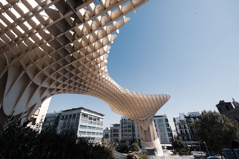 Close-up view of the Metropol Parasol structure in Seville, Spain, featuring its distinctive latticed wooden canopy against a blue sky.