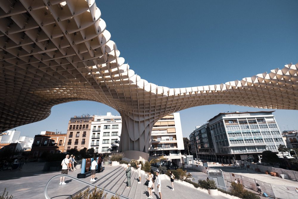 Close-up view of the Metropol Parasol structure in Seville, Spain, featuring its distinctive latticed wooden canopy against a blue sky.