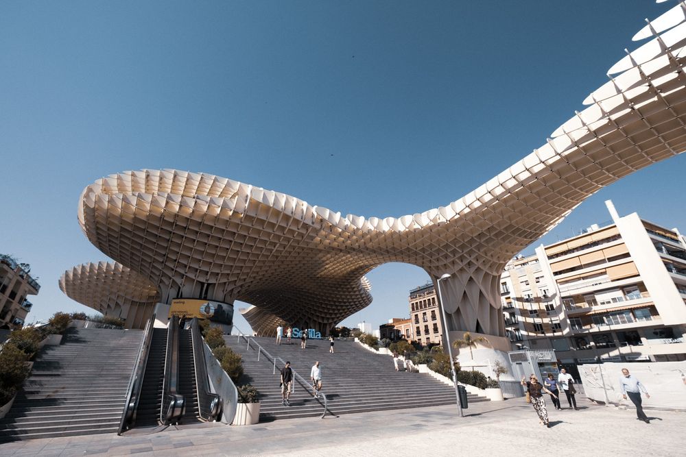 Close-up view of the Metropol Parasol structure in Seville, Spain, featuring its distinctive latticed wooden canopy against a blue sky.