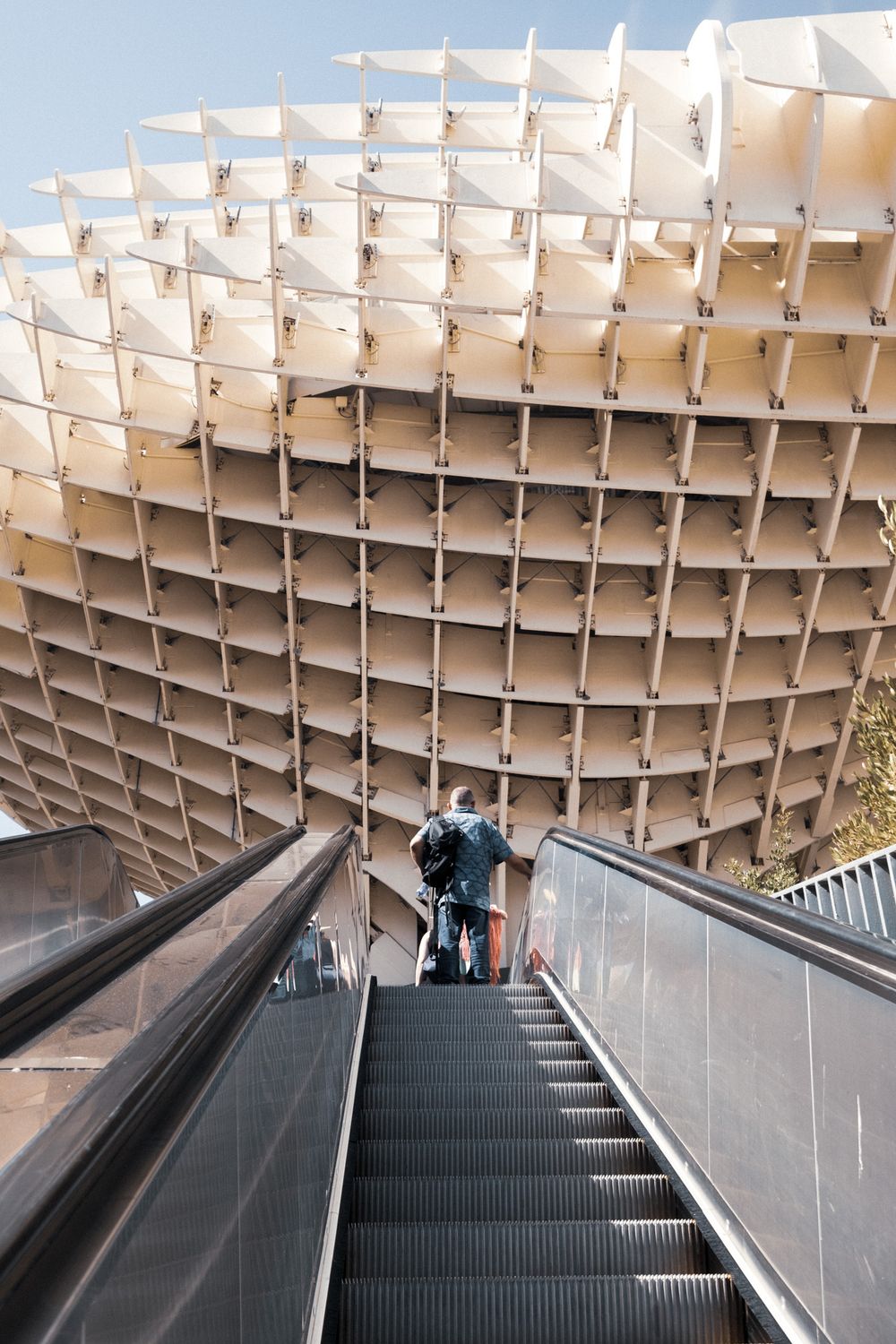Close-up view of the Metropol Parasol structure in Seville, Spain, featuring its distinctive latticed wooden canopy against a blue sky.