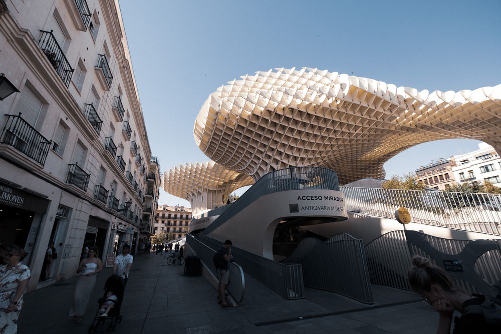 Close-up view of the Metropol Parasol structure in Seville, Spain, featuring its distinctive latticed wooden canopy against a blue sky.