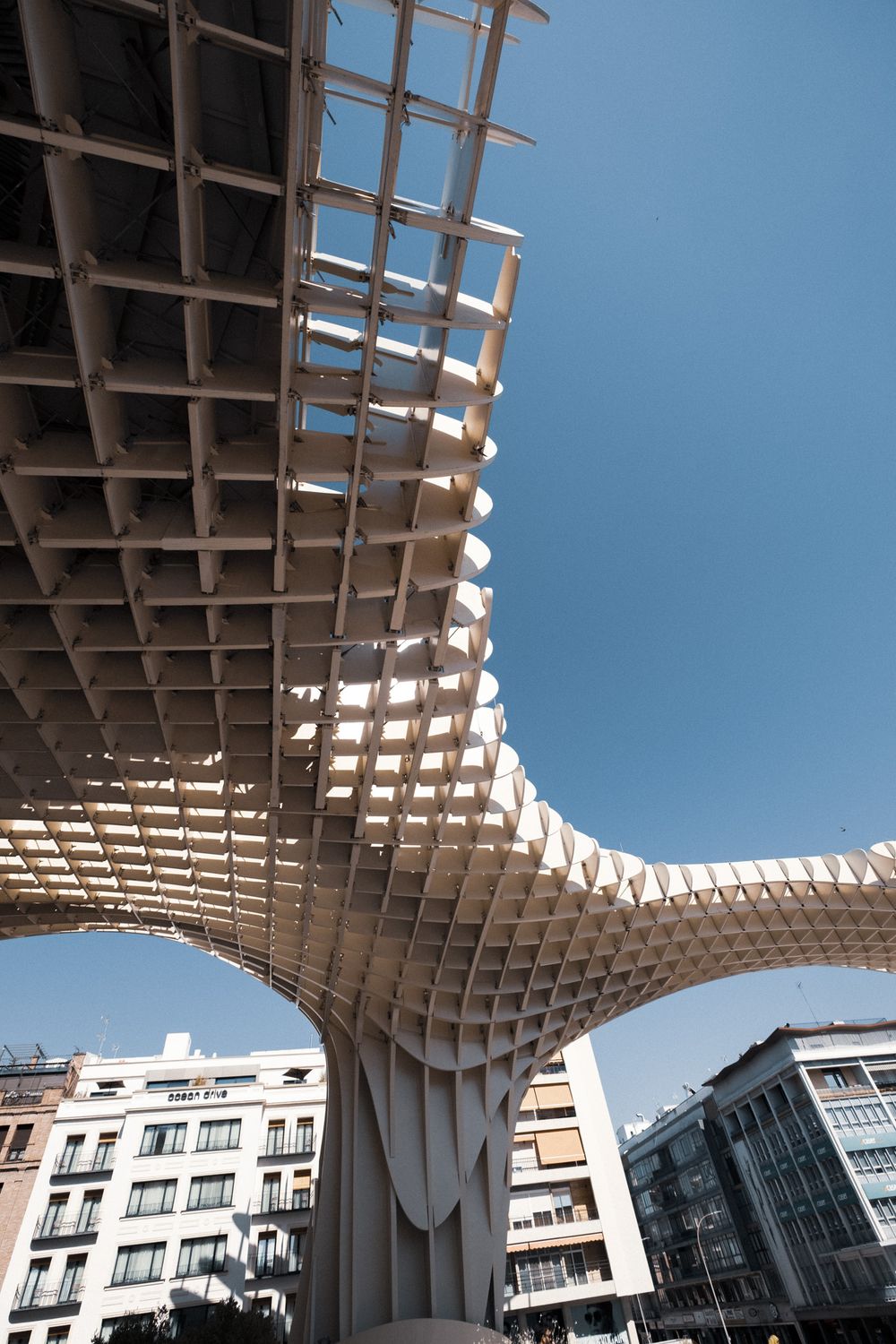 Close-up view of the Metropol Parasol structure in Seville, Spain, featuring its distinctive latticed wooden canopy against a blue sky.