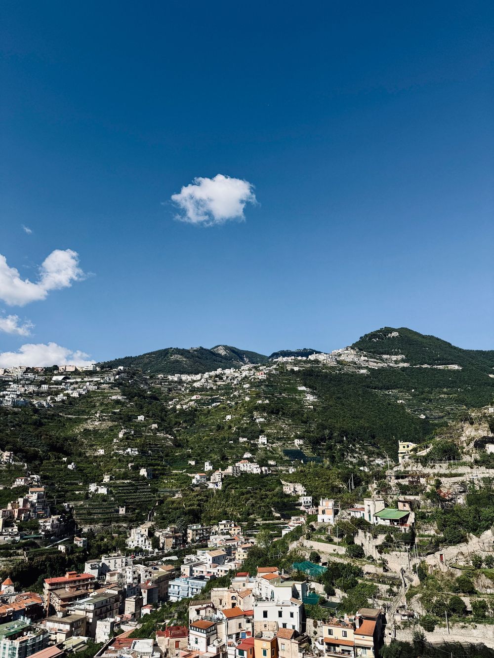 Colorful Italian hillside village with terraced gardens beneath a vivid blue sky on the Amalfi Coast.
