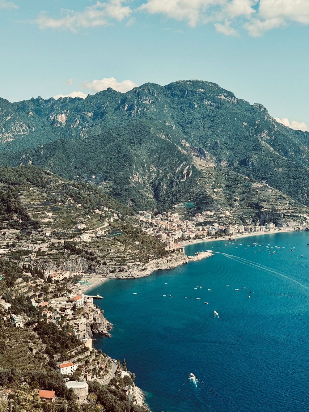 Breathtaking aerial view of Amalfi Coast town nestled between lush green mountains and vivid blue sea.