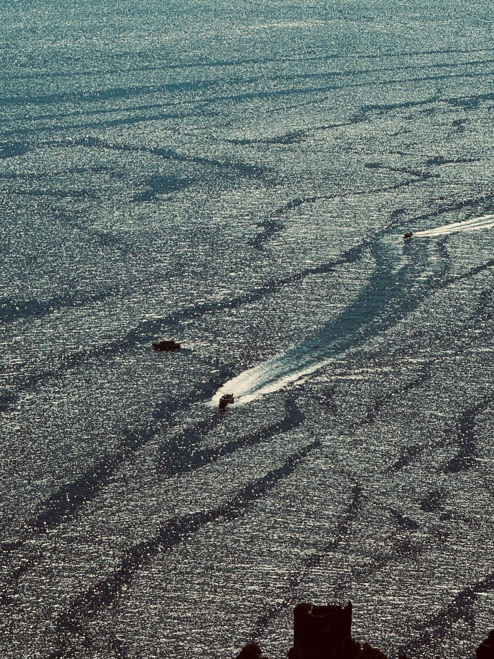 Aerial view of speedboats leaving white wake trails across sparkling sunlit Mediterranean waters.