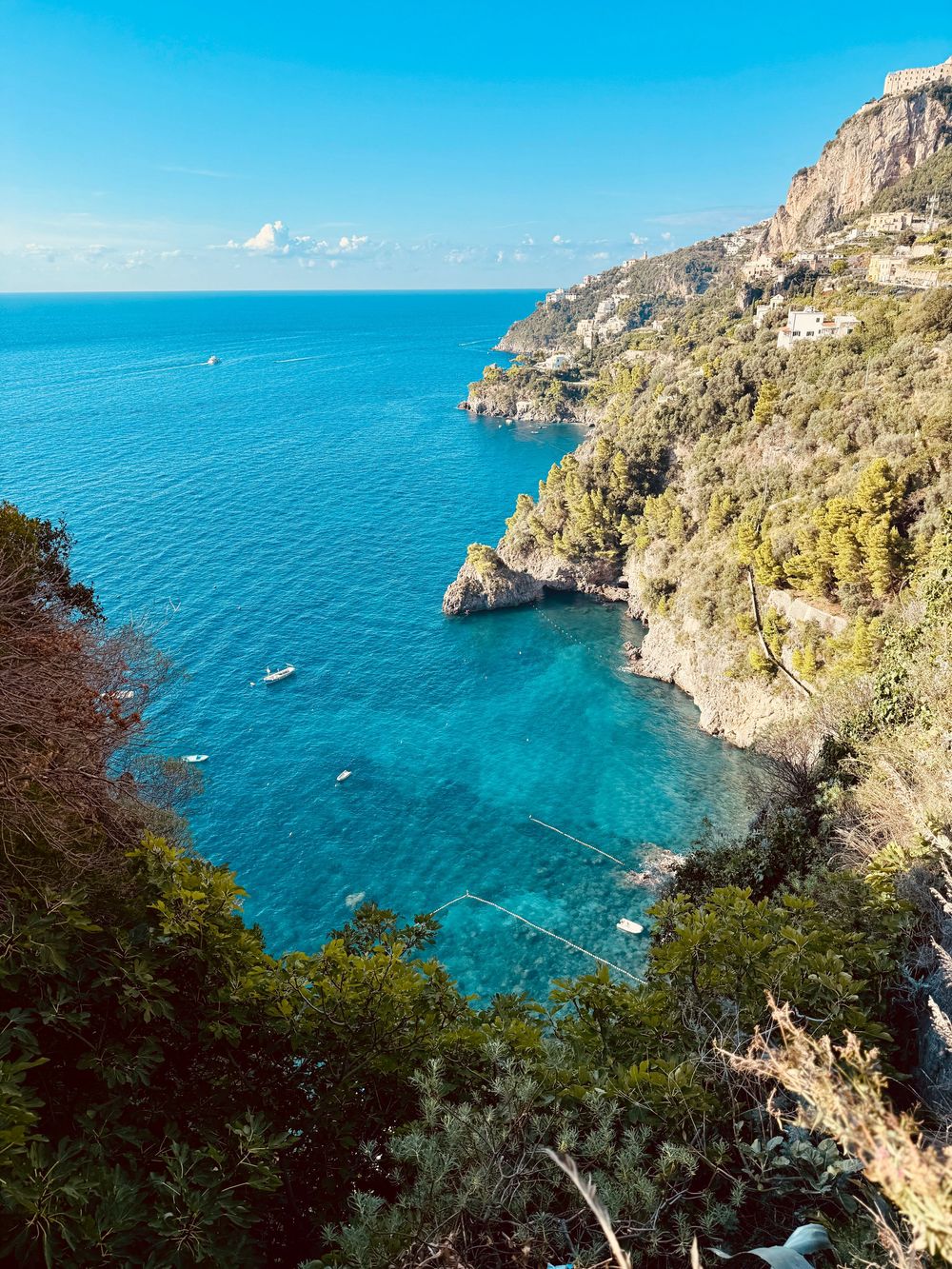 Crystal clear turquoise cove surrounded by dramatic rocky cliffs and lush greenery on the Amalfi Coast.