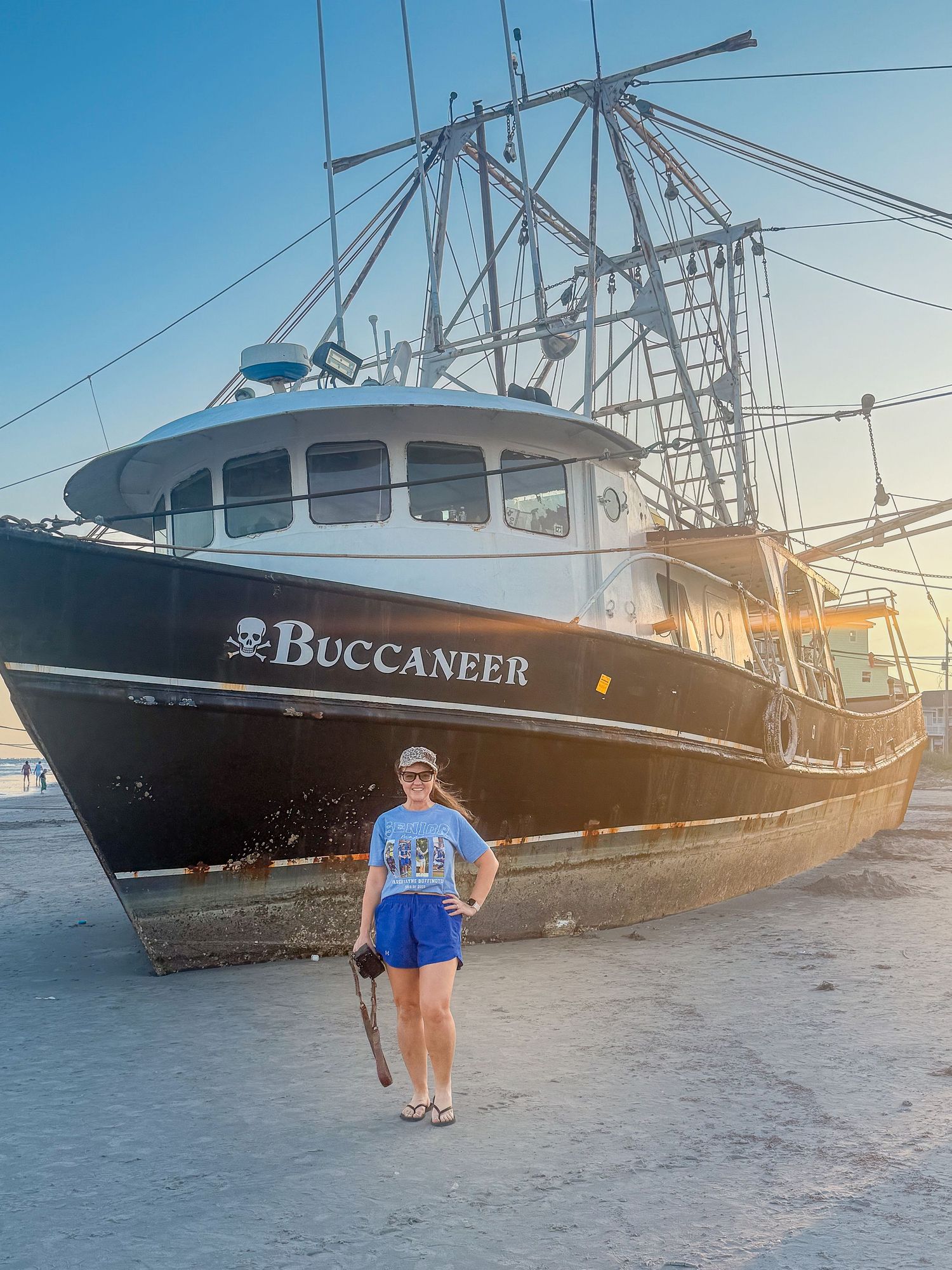 Woman standing in front of the Buccaneer fishing vessel docked at a sunny harbor.