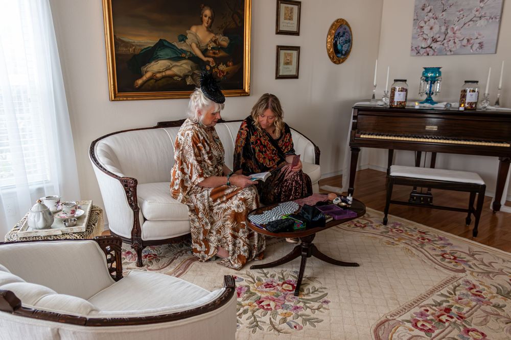 Two elderly women in floral dresses sit on a white sofa reviewing documents in an elegant living room.