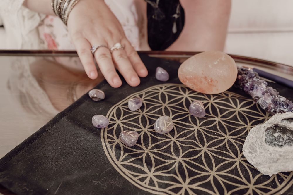 Hands arranging amethyst crystals on a Flower of Life grid board for crystal healing practice.