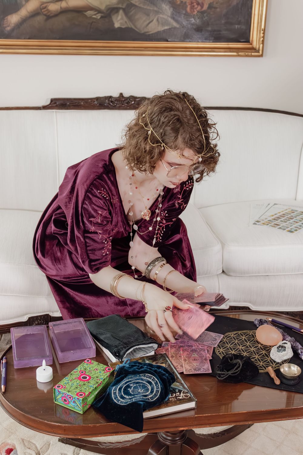 Fortune teller in purple velvet robe reading tarot cards at ornate table with crystals and mystical tools.
