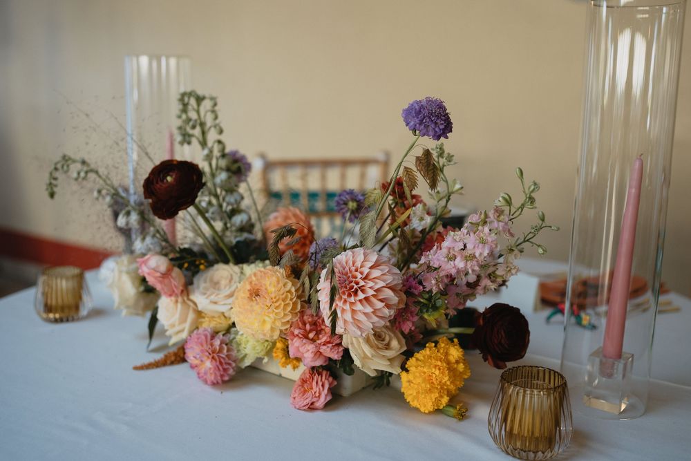 Colorful wildflower centerpiece with dahlias, thistles, and pink candles on a white tablecloth.