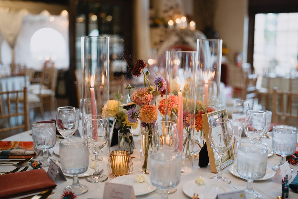 Elegant wedding reception table with pink taper candles, colorful floral centerpieces, crystal glassware, and warm ambient lighting.