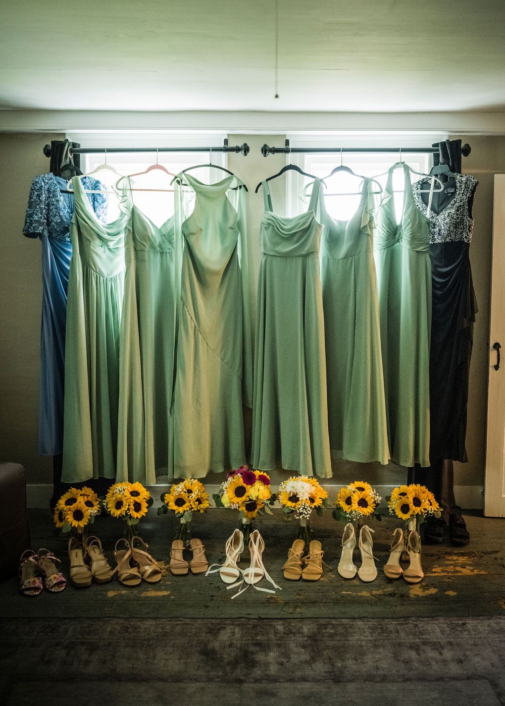 Sage green bridesmaid dresses hanging with sunflower bouquets and heels arranged below.