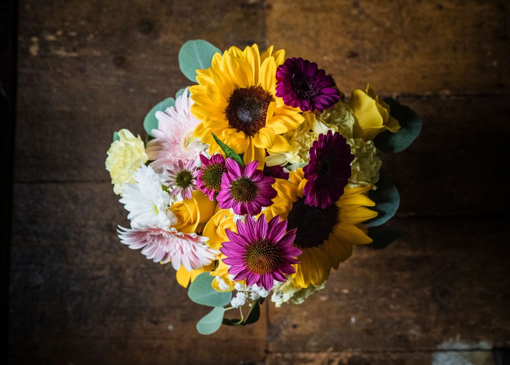 Vibrant wedding bouquet featuring sunflowers, purple gerbera daisies, and pink flowers on rustic wood.